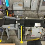 bag flattener conveyor discharges bags onto squaring conveyor for robotic bag palletizer