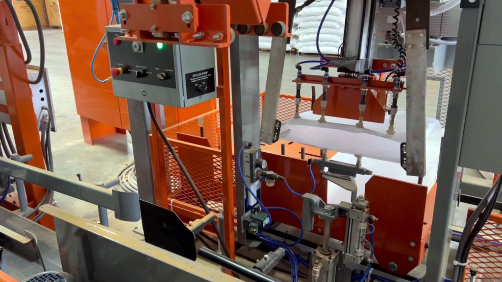 automatic bag placer picking up an empty bag and opening the mouth of the bag